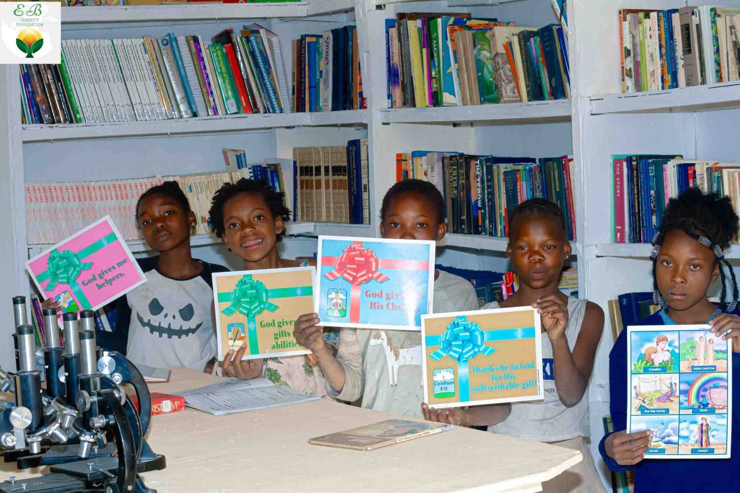 Children holding learning materials in front of the library shelves